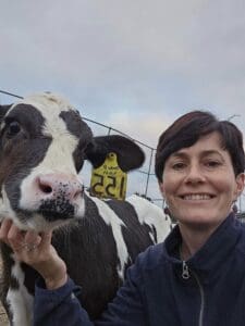 Julie MacGlaflin, smiling and scratching the chin of a black and white calf.