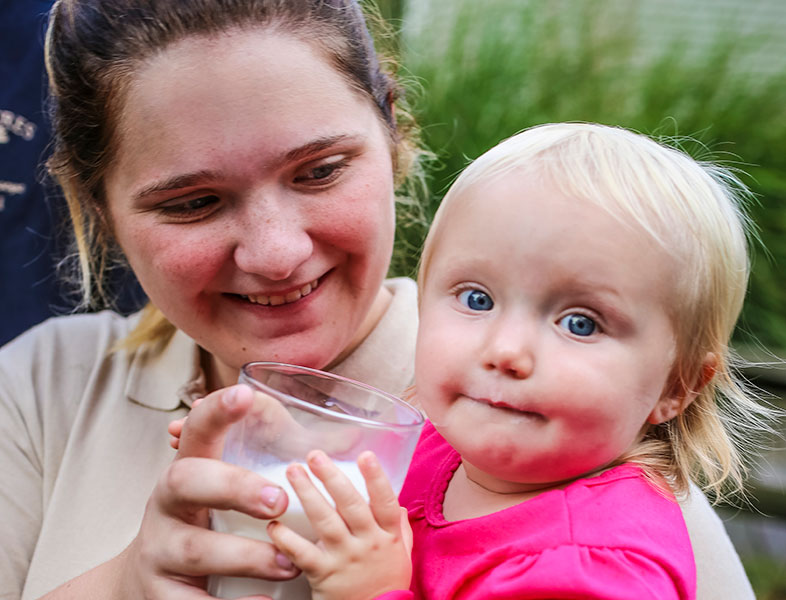 Woman holding a baby while they both hold glass of milk