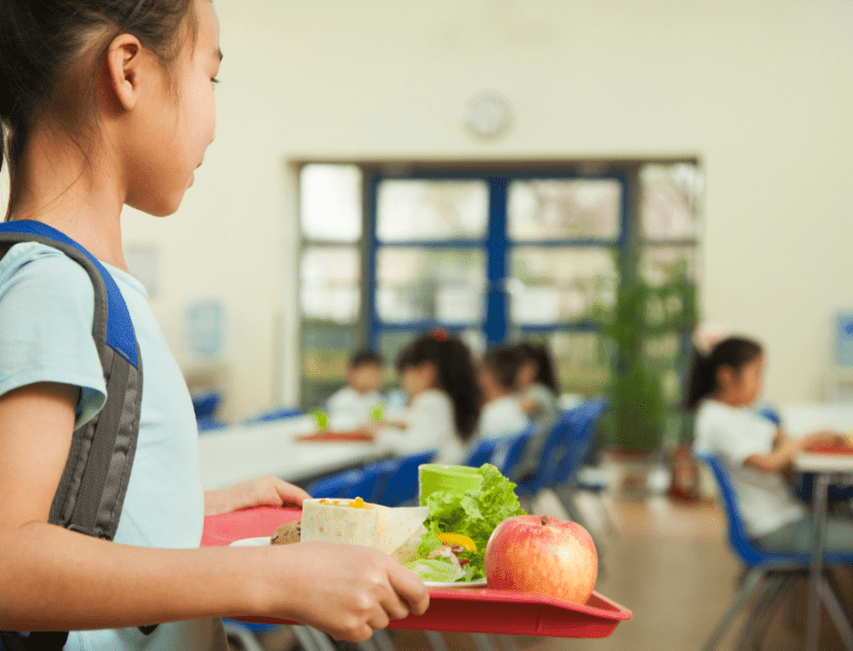 young girl holding lunch tray with apple