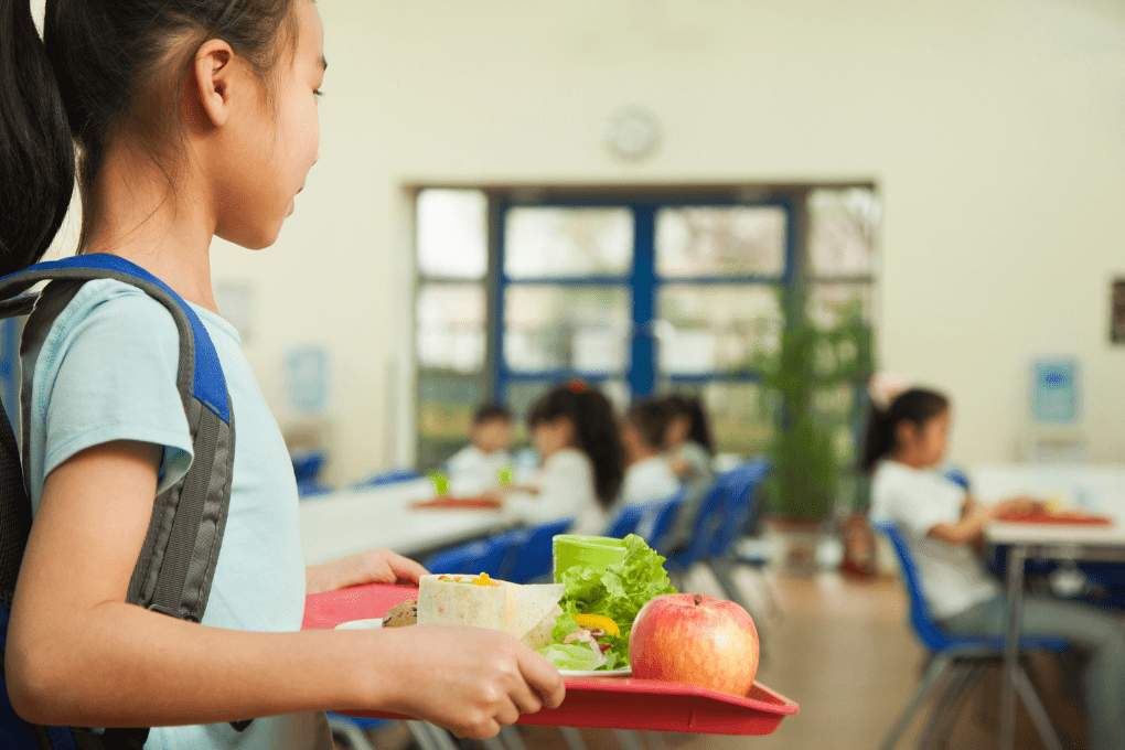 young girl holding lunch tray with apple