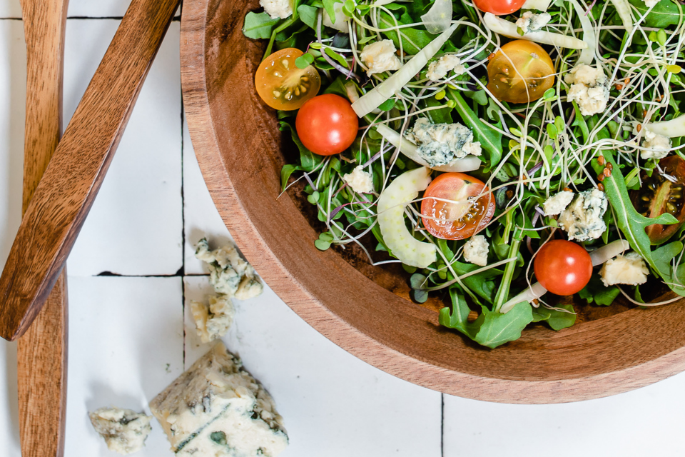 Partial shown wooden bowl of greens, tomatoes and blue cheese