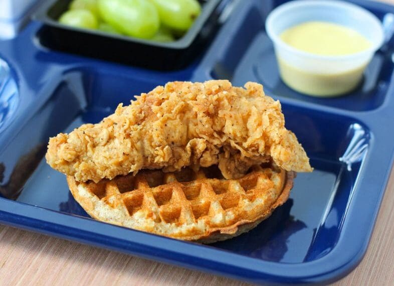 breaded chicken piece on waffle, honey mustard sauce and grapes on a tray