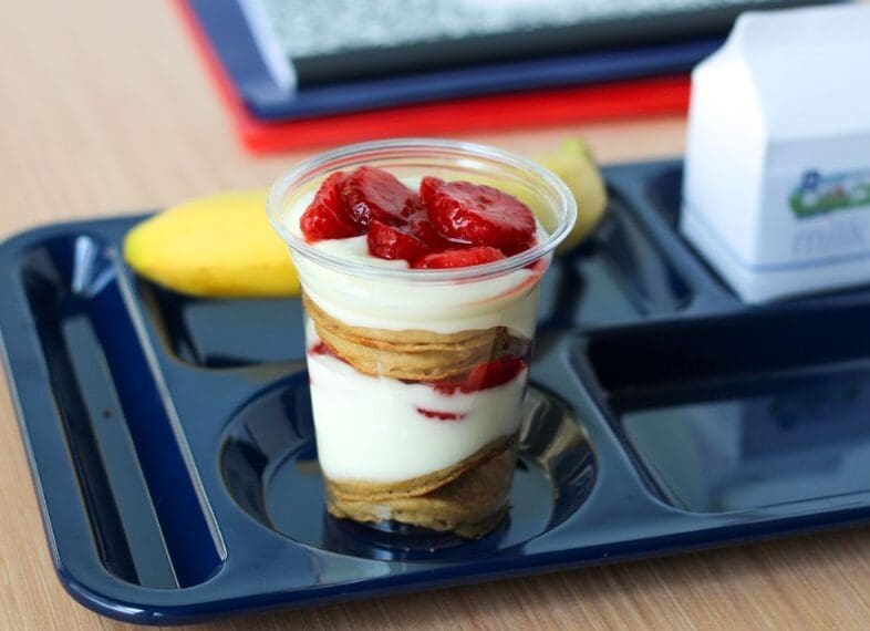 Layered pancake, yogurt and strawberry parfait on tray with banana and milk carton.