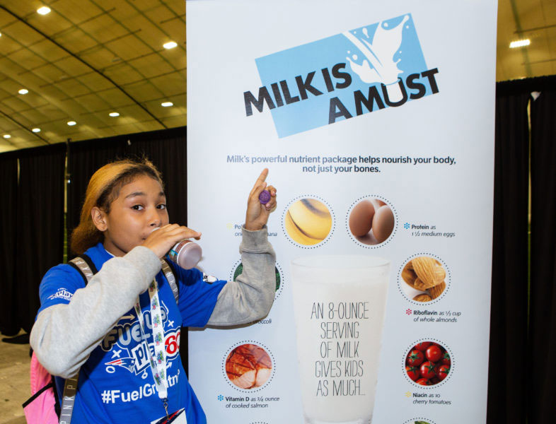 girl drinking chocolate milk pointing to sign saying "milk is a must"
