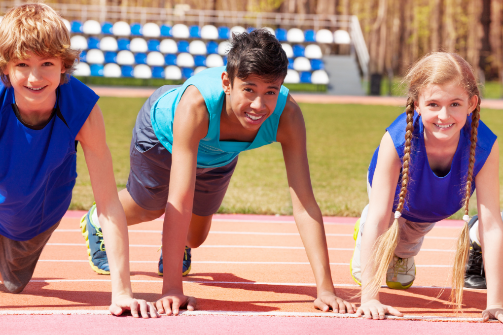 Three young athletes standing on starting line of track, ready to race.