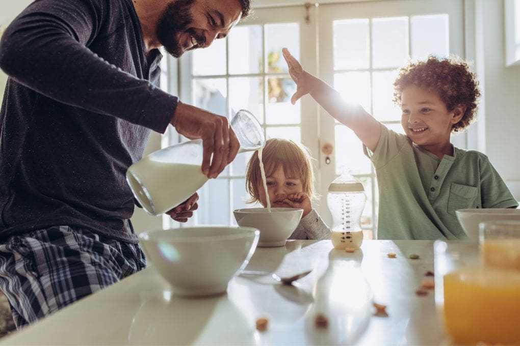 Parent pouring milk into cereal bowl for two children
